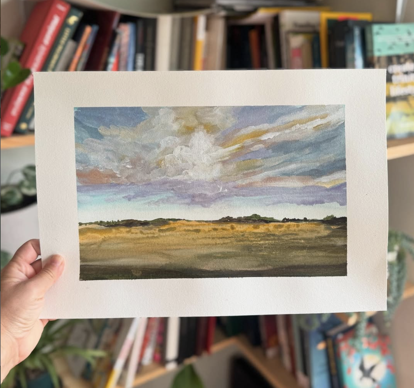 Watercolor painting of a prairie horizon under a big cloudy sky, held in hand